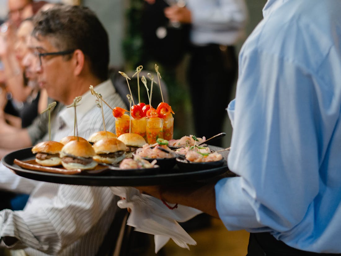 Campus catering staff serving food at a university event - trays carried through a campus dining space.