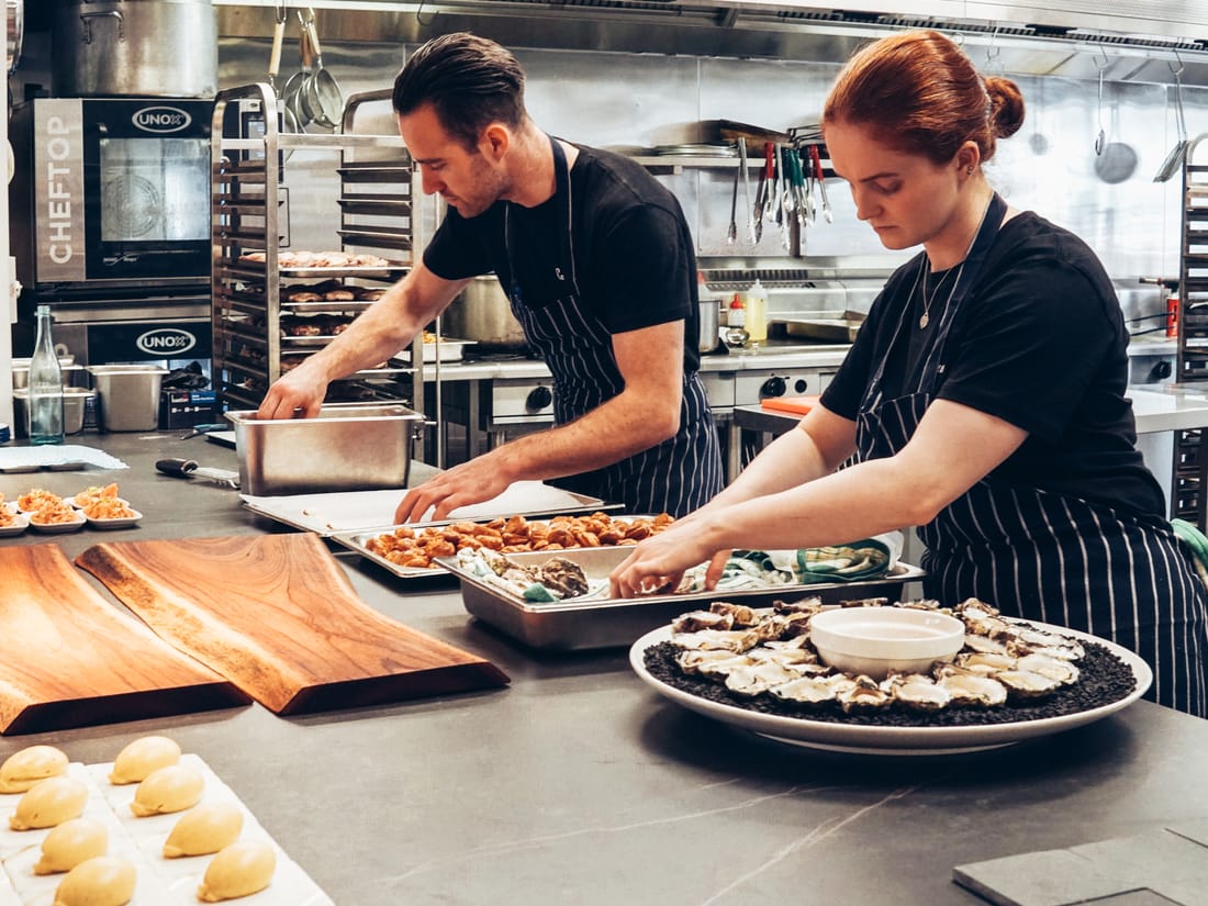 A small catering team preparing food together in a kitchen - the kind of lean, focused operation Catertoo is built for.